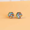 A pair of handpainted Rubik's Cube stud earrings in vibrant multicolor on a yellow background.