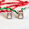 Two small animal earrings with Santa hats on a white surface with red and green ribbons in the background.