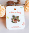 Pin badge of a plant design on a 'Robin Valley' branded card with decorative elements in the background.