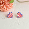 Heart-shaped Union Jack earrings on a light surface with a pink flower in the background