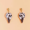 A pair of wooden earrings with a hand-painted design resembling a melting skull ice cream cone, attached to gold-colored hooks.