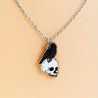 A wooden necklace with a pendant featuring a hand-painted raven perched on a skull, attached to a stainless steel chain.