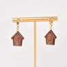 Pair of gingerbread house earrings on a gold T-bar against a light background